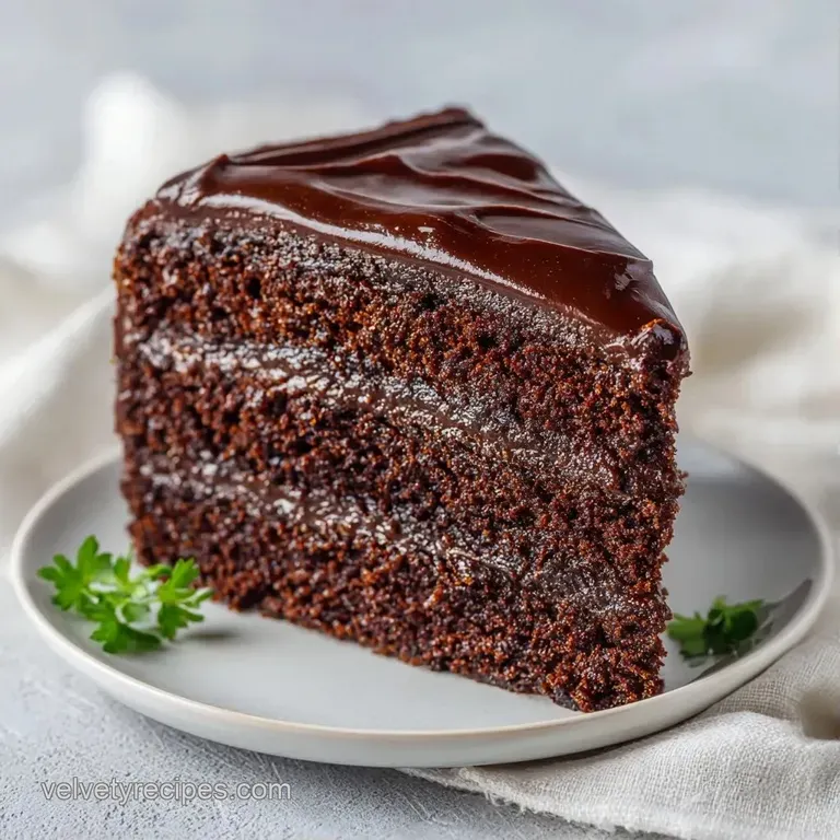 A neat slice of dark chocolate cake on a white porcelain plate, garnished with a red raspberry and mint leaf.